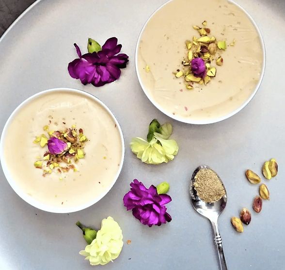 Zwei Schalen mit Joghurt, dekoriert mit Pistazien und bunten Blumen